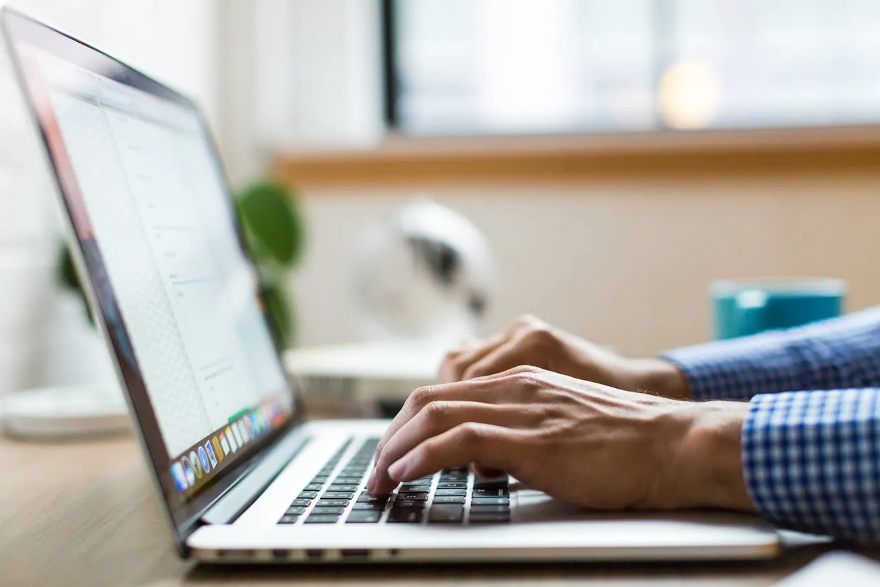 Close-up of someone typing on a laptop, with a blurred background suggesting an indoor workspace, possibly a home office.